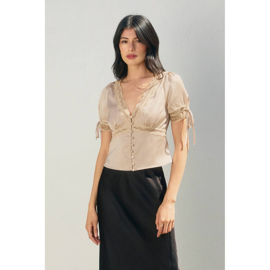 Woman wearing a beige blouse with short sleeves and a black skirt on a gray background